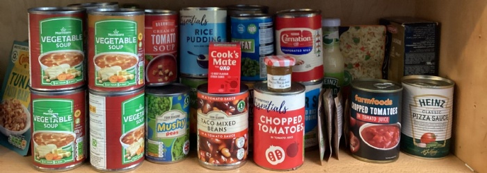 A photograph of assorted tinned food and jars on a wooden shelf.